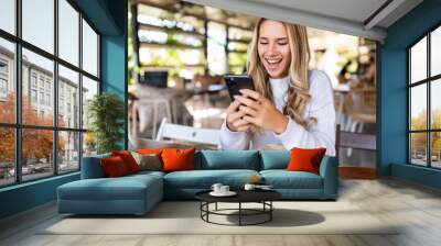 Young freelancer woman uses a mobile phone and laptop works in a cafe Wall mural